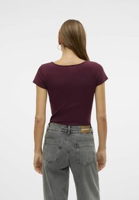 T-shirt bordeaux à manches courtes avec un col rond, associé à un jean gris taille haute avec une étiquette en cuir sur la ceinture arrière.