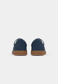 Zapatos de ante azul marino con un acabado texturizado, que presentan un acento blanco y una suela de goma marrón. Diseño simple y de perfil bajo con un talón liso.