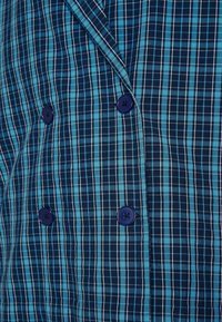 Modrý a tyrkysový kostkovaný textil s hladkým povrchem, se zapínáním na dvou řadách a pěti tmavě modrými knoflíky.