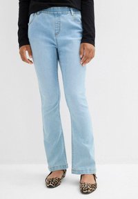 Jeans a zampa d'elefante azzurri chiari con una cintura elastica, caratterizzati da una texture liscia e cuciture a contrasto. Abbinati a ballerine con stampa leopardata.