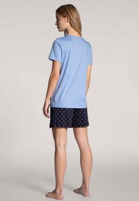 Lichtblauw T-shirt met korte mouwen en een ronde hals, gecombineerd met marineblauwe shorts met een klein wit wolkenpatroon, gezien van de achterkant.