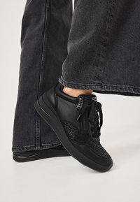 Baskets noires avec une surface texturée, présentant un cuir lisse et des coutures d'accent. Comprend un détail de fermeture éclair et une semelle en caoutchouc robuste.