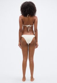 Λ ευκό μπικίνι με λαιμόκοψη halter και σχέδιο με δέσιμο στην πλάτη. Μαλακό, υφασμάτινο και υφή. Μίνιμαλ κάλυψη με ψηλές πλαϊνές περικοπές.