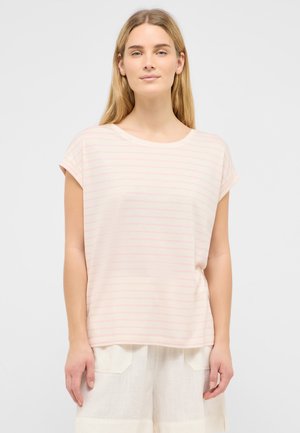 Woman wearing a light pink striped short-sleeve shirt and white shorts, standing against a plain light gray background.