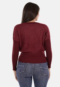 Maglione bordeaux con retro texturizzato e polsini a costine. Design a vestibilità ampia con vita arricciata, abbinato a jeans in denim scuro.
