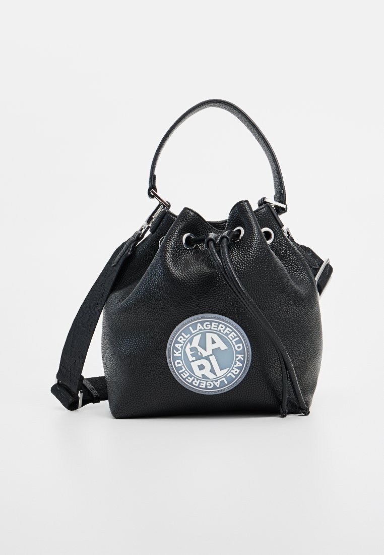 Schwarze strukturierte Bucket-Bag mit einem runden Logo-Patch. Verfügt über einen obigen Griff, einen Kordelzugverschluss und einen abnehmbaren Schulterriemen.