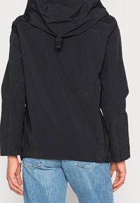 Schwarze wasserdichte Jacke mit Kapuze, ausgestattet mit einem Kordelzug am Hals und einem lockeren Schnitt. Das Material hat eine glatte, matte Textur.