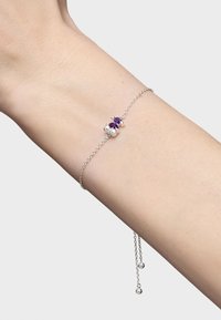 Pulsera de cadena de plata con una gema central morada y dos acentos esféricos, ajustable con una delicada cadena y extremos en forma de bola.