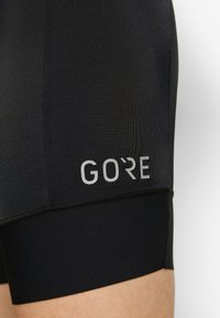 Czarne spodenki do jazdy na rowerze GORE wykonane z elastycznego materiału. Charakteryzują się eleganckim wzornictwem z odblaskowym logo i płaskimi szwami dla większego komfortu.