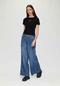 Schwarzes kurzärmeliges T-Shirt mit einem Sonnenmotiv über der Brust, kombiniert mit hellblauen Denim-Jeans im weit geschnittenen Stil und vorderen Taschen.