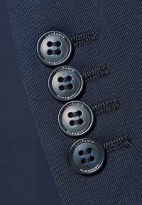 Szczegół marynarki w kolorze granatowym z czterema czarnymi guzikami, prezentującej dwudziurkowy design i szyte dziurki na guziki, wykonanej z materiału o teksturowanej powierzchni.