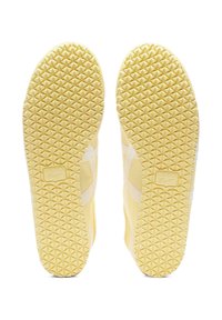 Żółte podeszwy sneakersów z teksturowanym, diamentowym wzorem na gripie i bocznymi paskami; wytłoczone logo na pięcie.