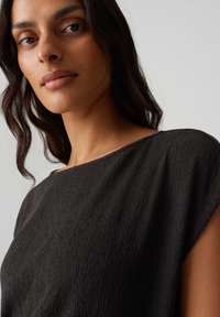 Zwarte textuurtop met een wijde halslijn en korte mouwen, met een gekreukt materiaal dat dimensie en visuele belangstelling toevoegt.