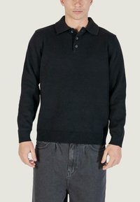Pullover nero lavorato a maglia con colletto, tre bottoni e polsini e orlo a coste. Il materiale ha una consistenza liscia. Abbinato a jeans scuri.