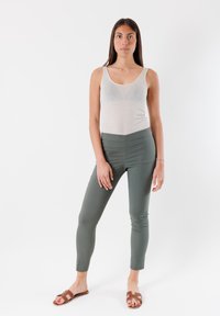 Canotta grigia chiaro con spalline sottili, abbinata a pantaloni aderenti verde scuro. Sandali piatti marroni con un design a fascia completano l'outfit.