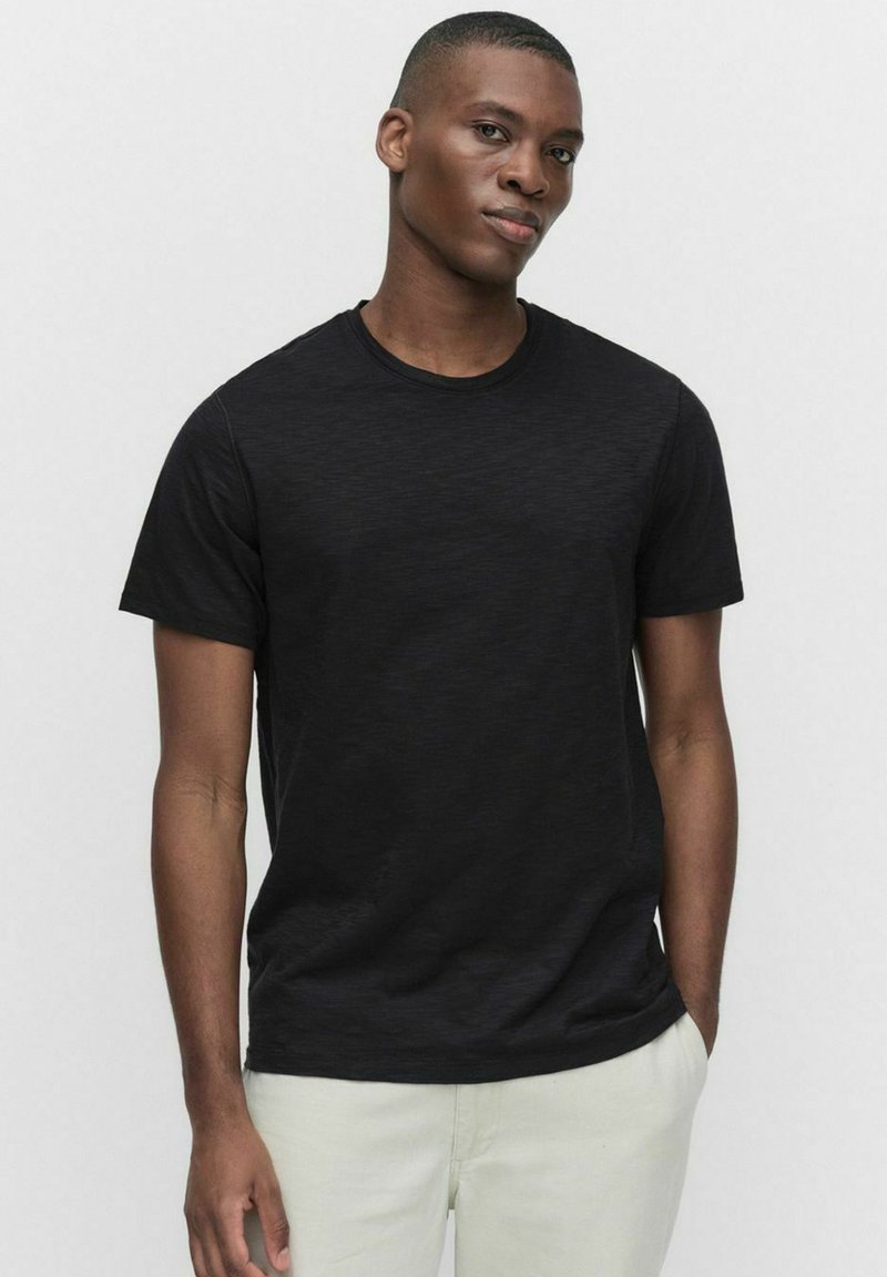 Sort kortærmet t-shirt lavet af tekstureret stof, med rund hals og en almindelig pasform, parret med lyse bukser.