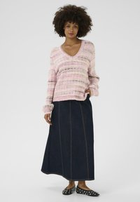 Rozā un krēmkrāsas svītrainā adītā džemperis ar V veida kakla izgriezumu, apvienots ar garu tumšo džinsu svārku ar redzamu šuvju. Melni dzīvokļi ar uzdūrēm.