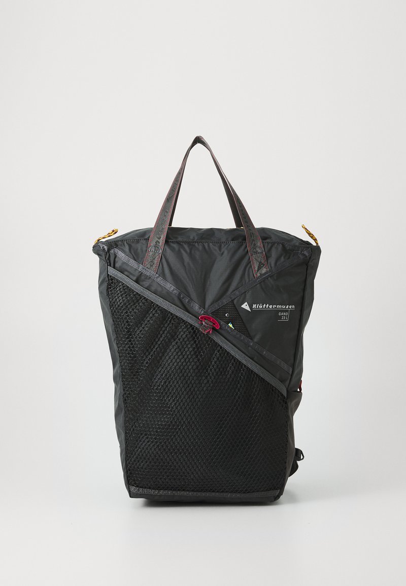 Svart ryggsekk laget av slitesterk nylon med en mesh frontlomme og kontrasterende røde detaljer. Har to solide håndtak og glidelås.