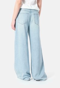 Lyseblå vide jeans har høy midje, to baklommer og en myk denimtekstur. Bunnlinjen er løs og faller over skoene.