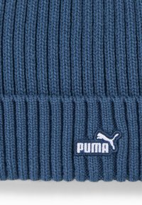 Gorro de punto azul con canalé vertical, que presenta un parche del logo de Puma en blanco sobre un fondo azul oscuro. Tela suave y texturada.