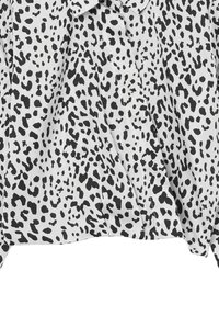 Blusa bianca con macchie leopardate nere irregolari, dotata di scollatura rotonda e maniche lunghe.
