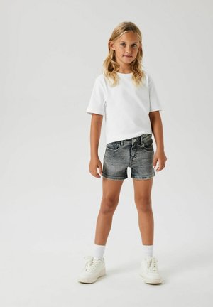 T-shirt blanc à manches courtes et short en denim gris. Le modèle porte des baskets blanches avec des semelles texturées et des chaussettes blanches. Design simple, coupe décontractée.