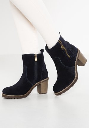 Bottes cheville en daim bleu marine avec talon bloc et fermeture éclair latérale, ornées de coutures décoratives et d'une semelle en caoutchouc texturée.