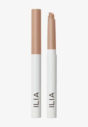 Deux sticks correcteurs ILIA avec un embout blanc et un capuchon beige, l'un fermé et l'autre ouvert montrant la pointe biseautée du correcteur.