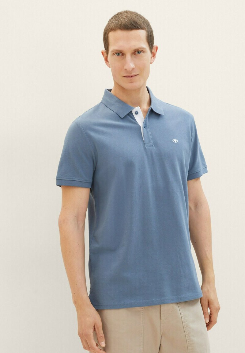 Blaues Polohemd mit kurzen Ärmeln, weißem Kragen und kleinem Logo auf der Brust, aus glattem, leichtem Stoff gefertigt.