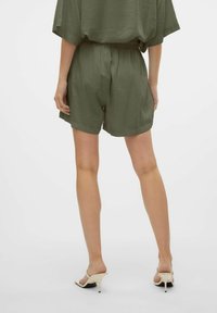 Pantaloni corti verde oliva con vita elastica, caratterizzati da un fit rilassato e una texture morbida. Indossati con sandali beige con tacco alto.