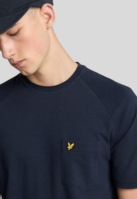 T-shirt in cotone navy con collo rotondo, maniche corte e design raglan. Presenta un piccolo logo giallo ricamato sulla tasca del petto.