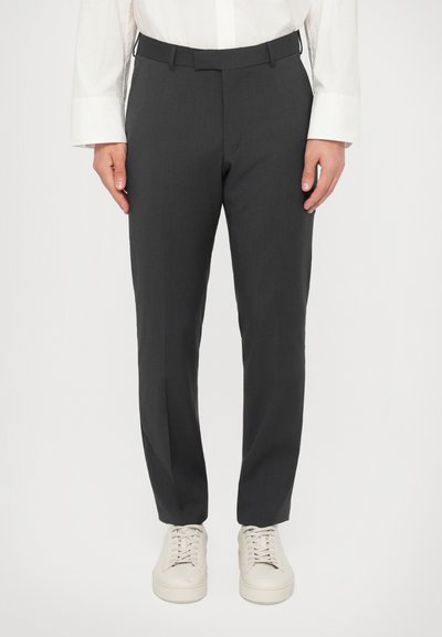 Pantalones grises a medida, elaborados con una tela suave, con un corte ajustado, trabillas para cinturón y bolsillos laterales, combinados con zapatillas blancas.