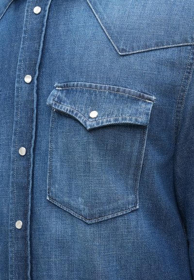 Camicia di denim di colore blu scuro con colletto a punta, bottoni a pressione argentati e una tasca sul petto con pattella.