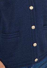 Cardigan bleu marine en maille texturée, ornée de boutons dorés, de deux poches plaquées et d'une bordure côtelée le long de l'ourlet.