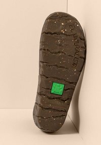 Suela de un zapato marrón oscuro con un agarre texturizado, pequeño cuadrado verde incrustado con un diseño de rana y la marca "EL NATURALISTA".