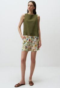 Top senza maniche verde oliva con orlo dritto, abbinato a pantaloni corti leggeri con un motivo floreale dai colori vivaci e una vestibilità comoda.