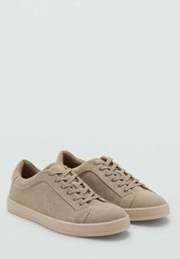 Beige Wildledersneaker mit runder Spitze, flachen Schnürsenkeln, einer strukturierten Oberseite und perforierten Details an der Seite. Gummisohle in einem passenden Farbton.