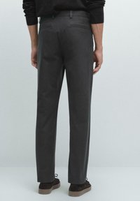 Gray trousers made of a smooth fabric, featuring a tailored fit, two rear pockets, and a discreet waistband. Worn with dark brown shoes.