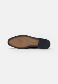 Suela de zapato de cuero marrón con una textura suave. Presenta un acento azul oscuro en el talón y estrías alternadas para tracción y flexibilidad.