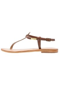 Hnědé kožené sandály na thong s úzkým designem řemínku, plochou dřevěnou podrážkou a nastavovacím zapínáním kolem kotníku. Lehké a minimalistické.