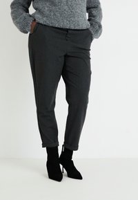Pantalones negros ajustados con puños enrollados, combinados con un suéter de punto gris. El conjunto presenta un corte clásico y bolsillos.