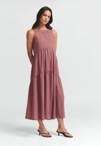 Mauve brezrokavnik obleka s flared, večstopenjsko zasnovo, gladko teksturo in dolžino do kolen. Ujemajoče se s črnimi petami.