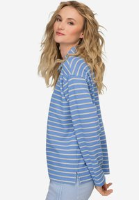 Jasnoniebieska, w pionowe paski, koszula z długim rękawem, z kołnierzykiem i bocznymi rozporkami. Materiał wydaje się być miękki i teksturowany, z delikatnymi beżowymi poziomymi paskami.