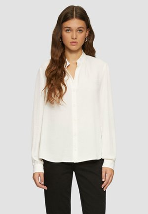 Witte blouse met lange mouwen en een sluiting met knopen aan de voorkant, zachte textuur en een licht gebogen onderrand. Voorzien van een staande kraag en een losse pasvorm.