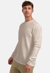 Világosbézs kötött pulóver texturált, vízszintes csíkozással, kör alakú nyakkivágással és bordás szegélyű mandzsettákkal. Puha, sima anyaga laza, kényelmes szabást biztosít.