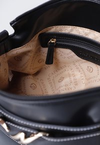 Sort læder håndtaske indvendig med cremet stofforing, indeholdende en lynlåslomme og et brandlogo mønster overalt. Hardware i guldfarve som accent.