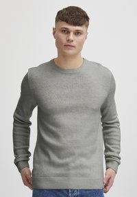 Pull en tricot gris clair avec un col rond, des manches longues et des bords côtelés aux poignets et à l'ourlet. Texture douce, coupe ajustée, détails minimes.