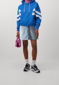 Felpa blu con strisce bianche, dolcevita rosa, gonna di jeans, borsa brillante rosa, calze bianche e sneaker nere con dettagli argentati.