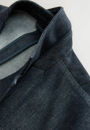 Veste en denim foncé avec un col structuré et une texture subtile. Présente une doublure gris clair et des coutures détaillées le long des coutures.