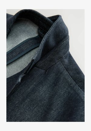 Donkerdenim jasje met een gestructureerde kraag en subtiele textuur. Het heeft een lichtgrijze voering en gedetailleerde stiksels langs de naden.